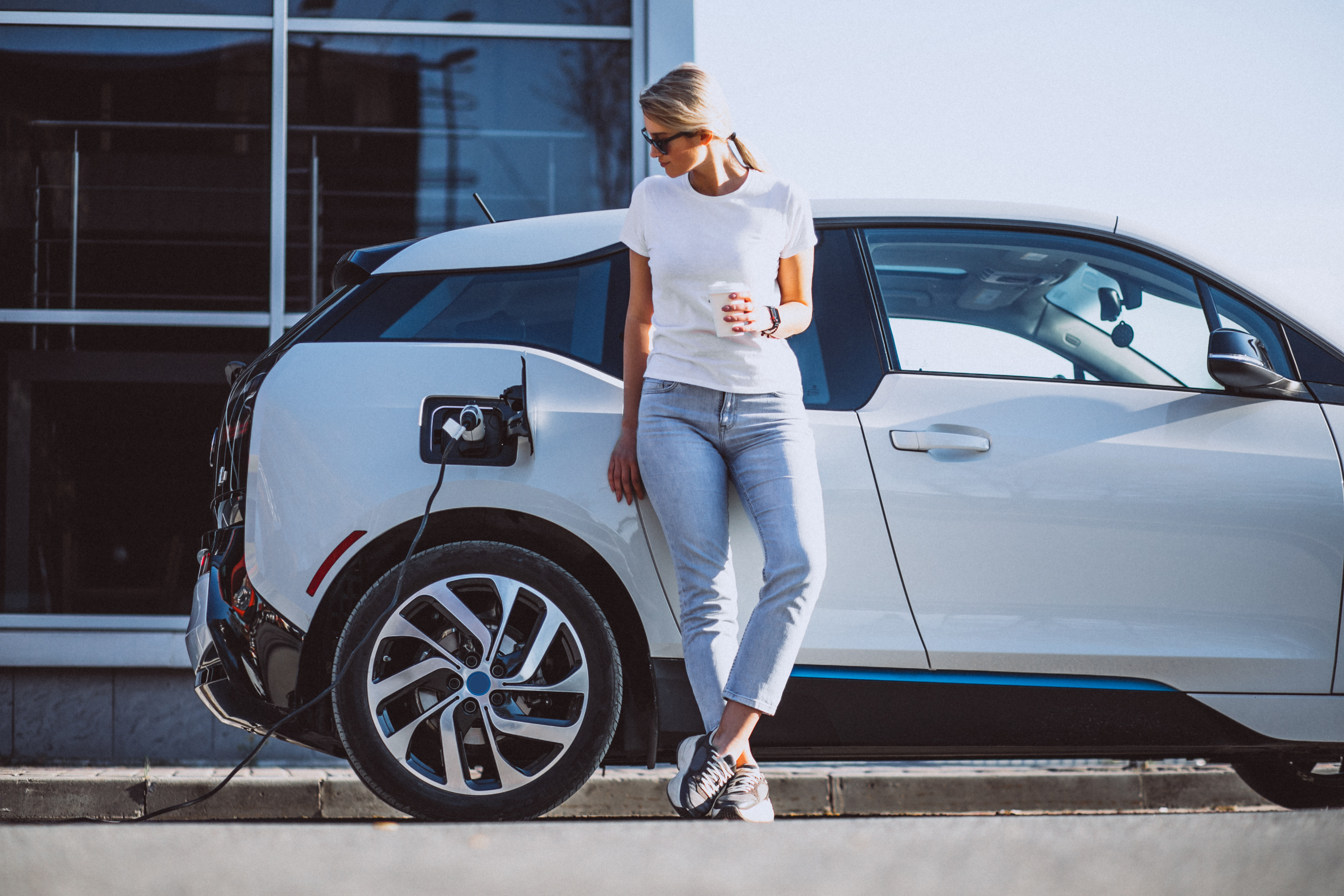 Woman leaning on charging car holding coffee